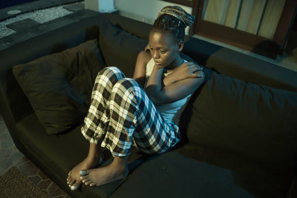 young Afro American woman suffering depression - sad and depressed black teenager girl in pain at home sofa couch feeling overwhelmed and emotional crying lonely in the dark
